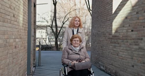 Woman Pushes Senior Woman in Wheelchair on City Street