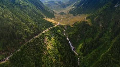Río que fluye a lo largo de la carretera en el valle y cae desde la ladera de la montaña verde.
