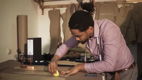 Male fashion tailor working on the measurements for the suit design in his workshop.
