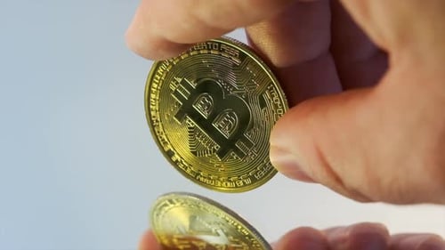 Close up golden bitcoin coin in fingers male hand on mirror surface cryptocurrency background.