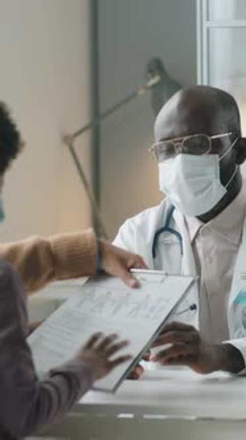 Pediatra afroamericano con máscara consultando a un niño y a su padre