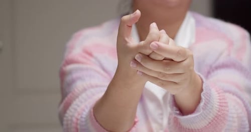 Eine Dame, die einen rosa-lila gestreiften Pullover trägt, kneift sich die Handknöchel und Finger, während Mama