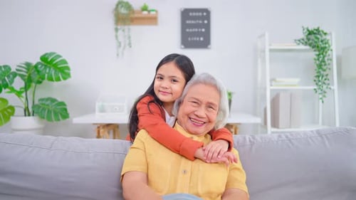 Smiling Girl Hugs Grandmother on Couch at Home