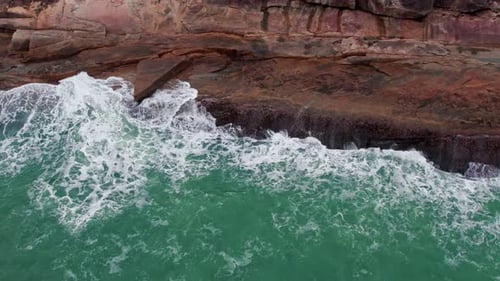 Aerial view of blue waves crashing on the rock pier in the sea.