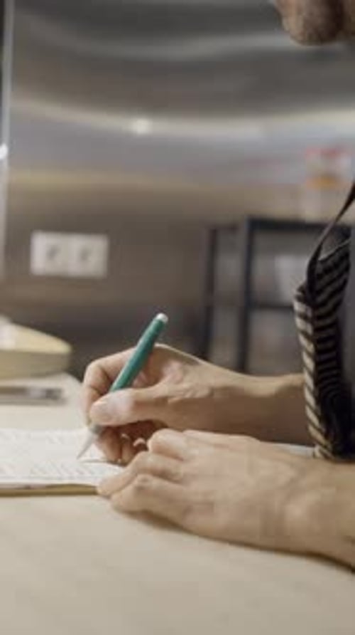 Close Side View of Male Chef Writing on Pad in Restaurant Kitchen