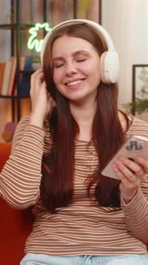 Smiling woman using phone with headphones indoors