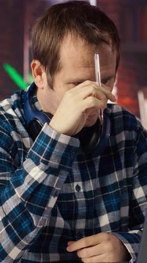 Stressed Man in Home Office Scratching Head with Pen Feeling Overworked