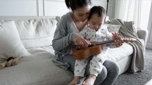 Mother and baby play ukulele on the couch
