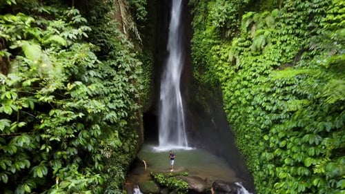 Aerial 4k: Young tourist male standing at Leke Leke Waterfall, Tropical Paradise hidden in a lush gr