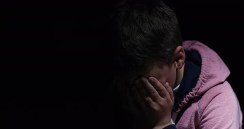 A scared little boy sitting in the darkness alone while crying