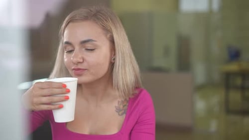 Portrait of Smiling Young Caucasian Woman Drinking Tasty Juice From Paper Cup in Cafe Positive