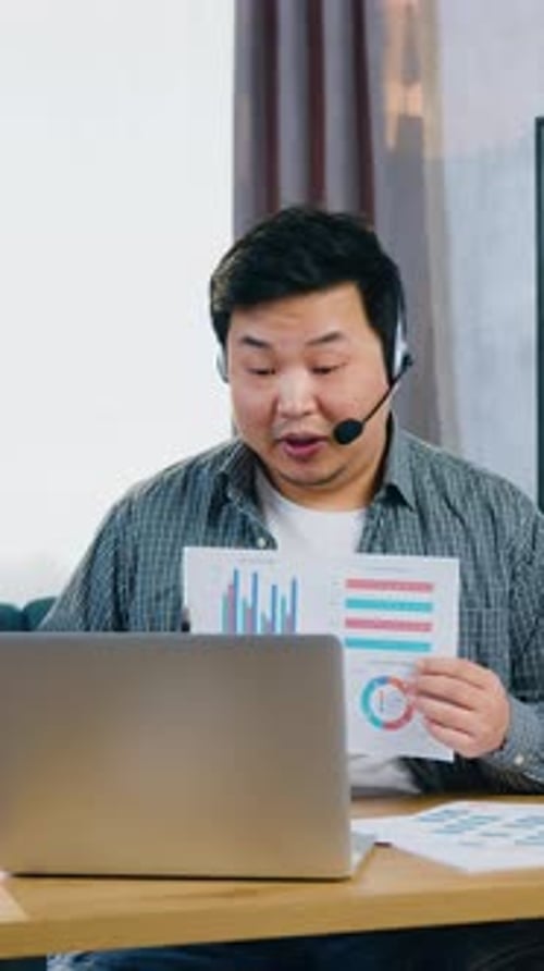 Handsome Experienced Confident Young Asian Man in Headset Sitting in Home Office Near Laptop and