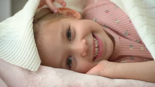 Menina se esconde debaixo do cobertor e ri Criança brinca na cama depois de dormir e tola