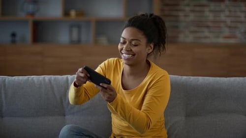 Joven mujer afroamericana feliz jugando Vídeo en un teléfono inteligente disfrutando del entretenimiento cibernético en