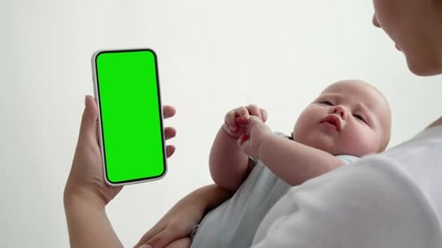 Young Mum with Little Baby Use Smartphone with Green Screen Chroma Key Closeup