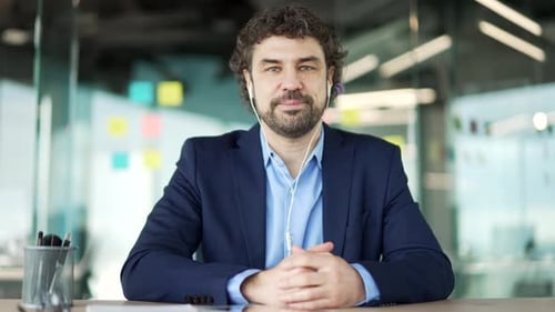 Webcam view. Businessman in headphones talking on a video call looking at camera sitting in office.