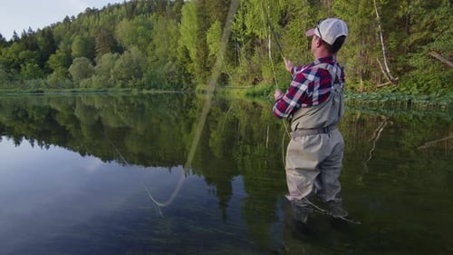 Fly fishing. Angler stands in the river and casts the fly at sunset. Fisherman fishing on fly