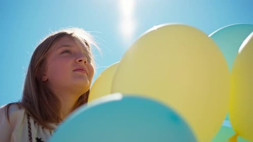 Bottom Angle View Cheerful Teenage Girl with Yellow and Blue Balloons in Sunrays Outdoors