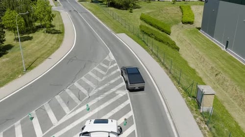 Aerial view following a modern EV car driving on a village road, sunny day