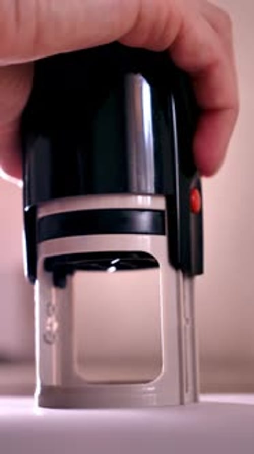 Hand Holding and Pressing a Black Stamp