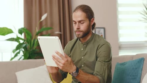 Man Uses Tablet While Sitting on Couch