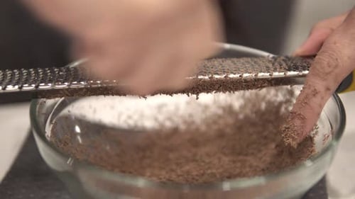 A young girl grates chocolate into a bowl for melting while making millionaire shortbread cookies wh