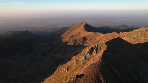 Golden sunlight over dramatic mountain peaks captured in aerial drone view