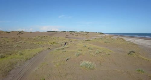 Man Driving ATV In The Dunes To The Beach. - aerial follow shot
