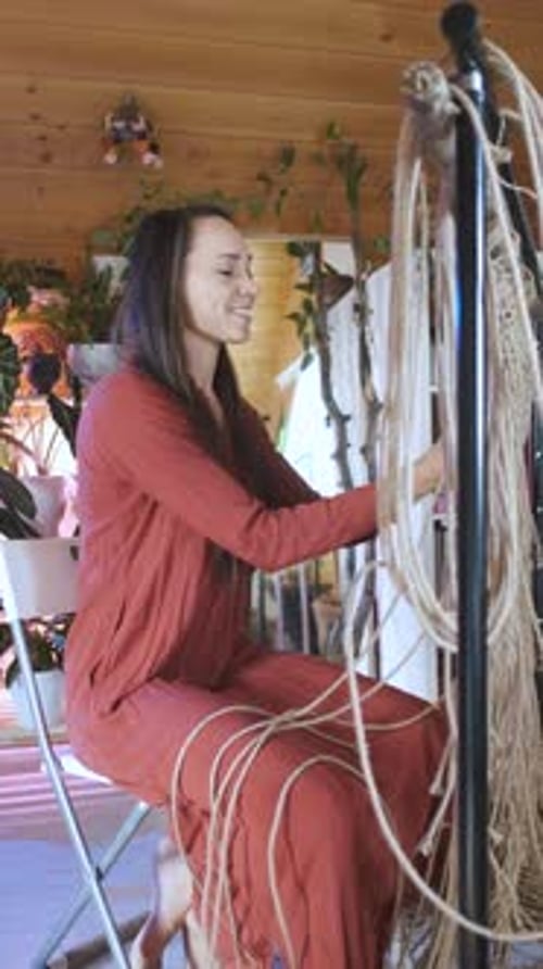 cheerful young woman weaves macrame while sitting at home