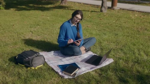 Konzentrierte Studentin, die im Autumn Park in ein Notizbuch schreibt