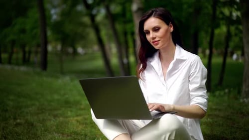 Beautiful Middle Age Woman Working at the Laptop As Sitting on Grass in City Park Student Studying