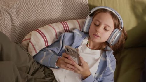 Girl with Headphones Lying on Sofa Using Smartphone