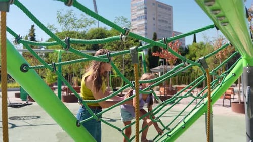 Mutter hilft Tochter beim Klettern auf die Seilkonstruktion des Spielplatzes