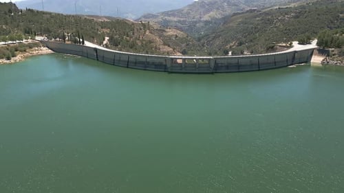 Vault dam. Panoramic aerial view in ascend of road over curved dam. Spain.