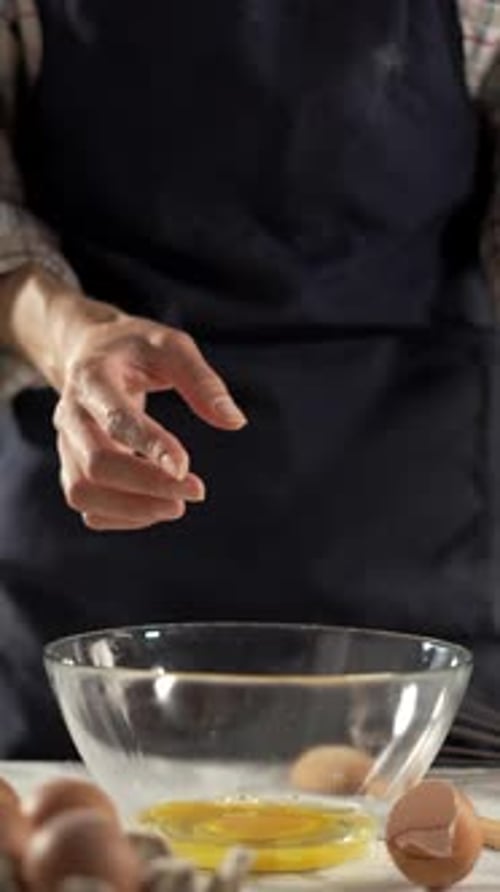 A chef is cracking eggs into a glass bowl as part of cooking preparation in a kitchen