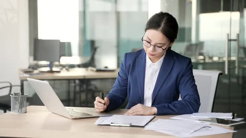 Confident asian businesswoman signing documents sitting at a desk at workplace in a business office.