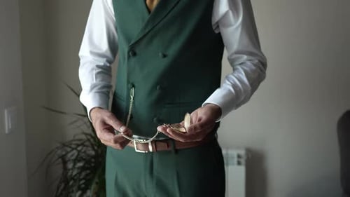 Groom adjusting green vest with pocket watch chain