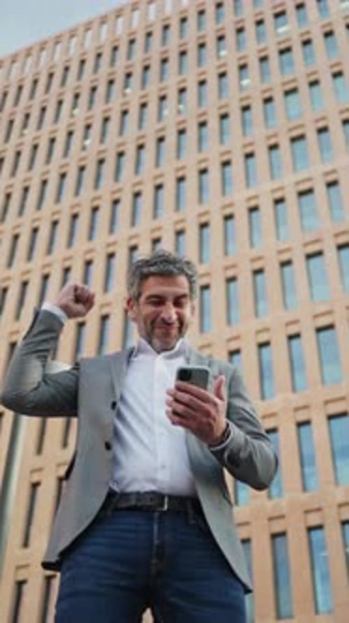 Businessman Celebrating Success with Smartphone in Urban Setting