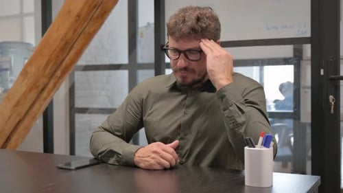 Stressed Man Rubbing Head at Office Desk