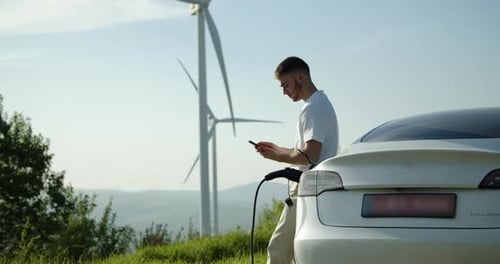 Man Charging Electric Car by Wind Turbines