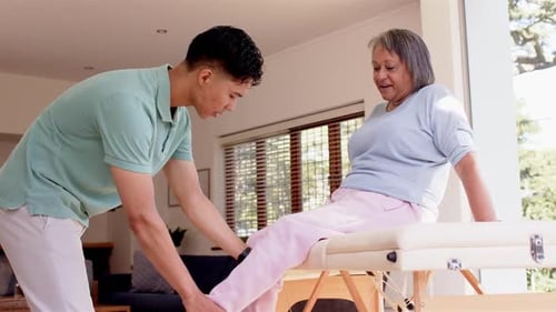 Young Therapist Helping Senior Woman With Leg