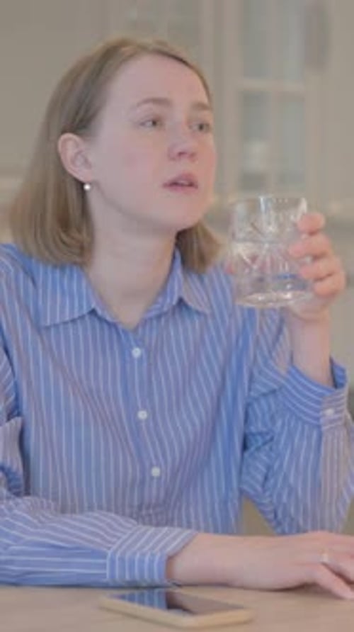 Woman Drinks Water at Table with Phone