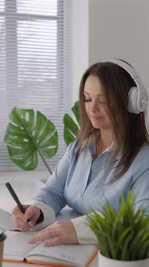 In Her Urban Home Office a Woman is Deeply Focused and Committed With Headphones on She Writes
