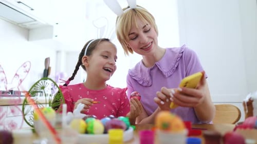 Girl Paints Easter Egg with Adult Using Phone