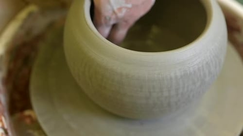 Potter hands applying finishing touch to completed handmade flowerpot on workshop pottery wheel