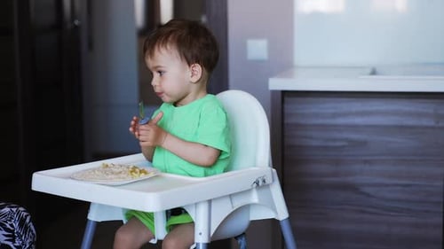Child Eating Food in High Chair with Fork