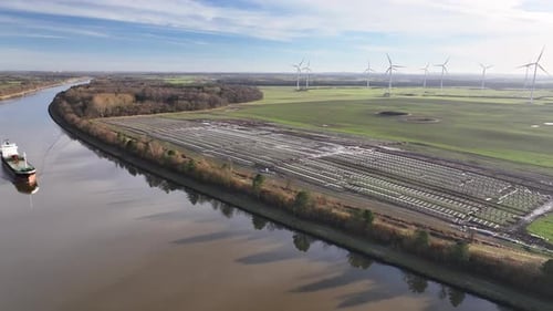 Footage of a construction site for a photovoltaic park with wind turbines in the background and a fr