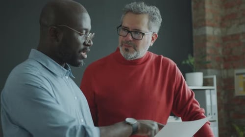 Senior Businessman Discussing Document with Young Colleague in Office