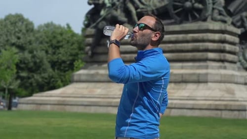 Man Resting and Drinking Water After Jogging in City Park, Super Slow