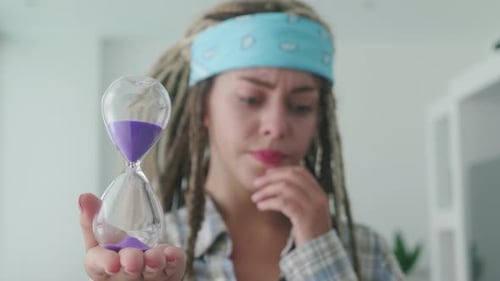 Selective Focus on an Ancient Hourglass with Flowing Colored Sand in the Hands of a Young Hipster
